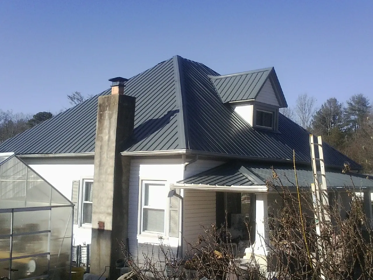 Dark blue standing seam metal roof on a white farmhouse with dormer — Slate & Tile Roof Repair by Roofing Brothers in La Junta