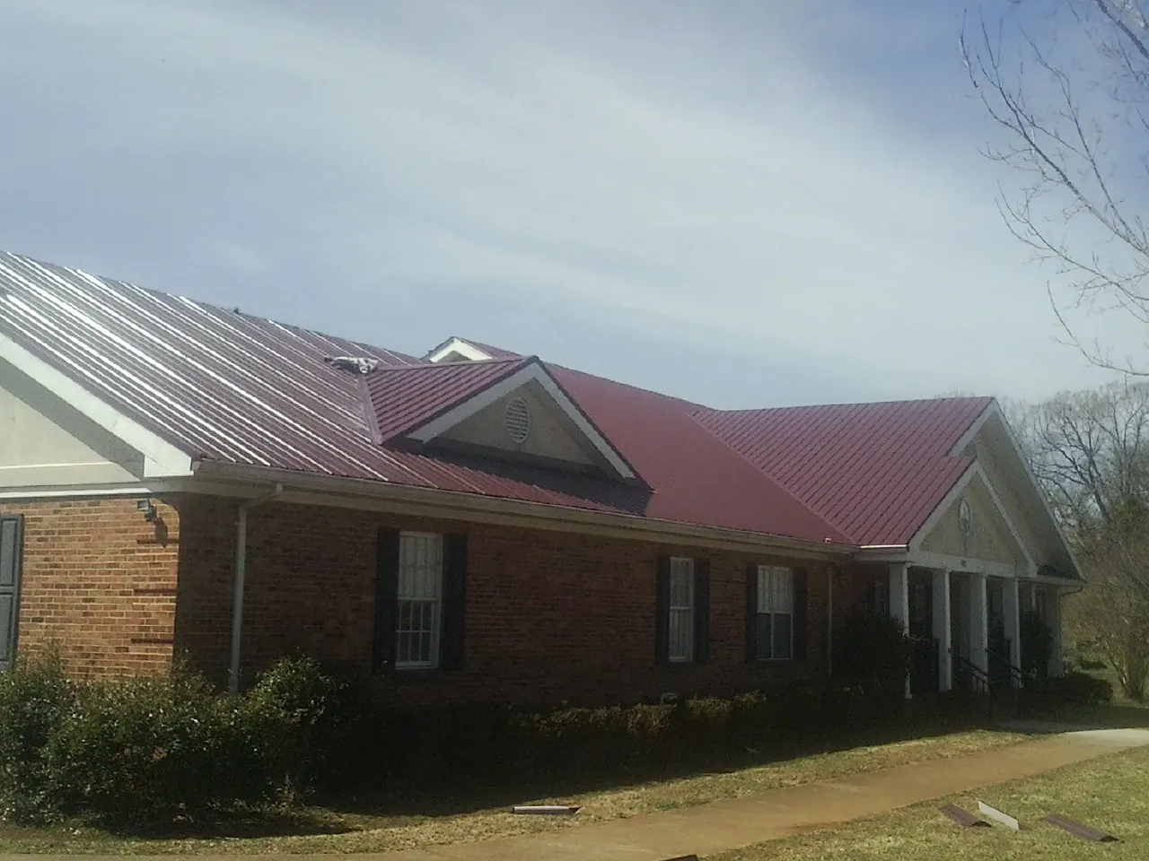 Red metal roof with gabled entries on a long brick building, from a Hail Damage Roof Repair job in La Junta