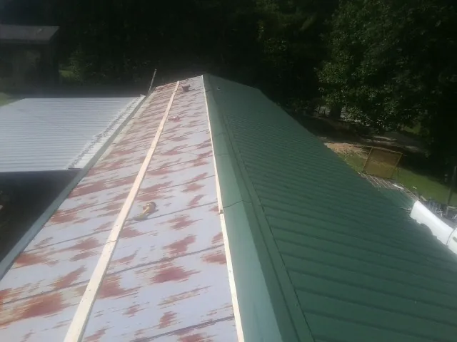 Old rusted panels beside newly installed green metal roofing — Wind Damage Roof Repair by Roofing Brothers in La Junta