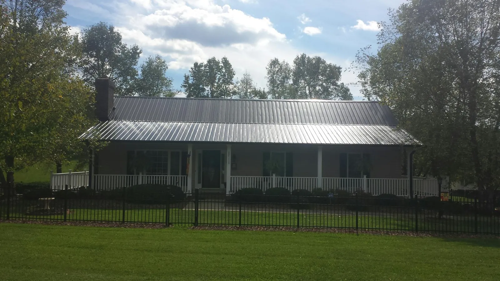 Gray metal roof on a brick ranch with a full width front porch — Gutter Guard Installation work by our crew in La Junta